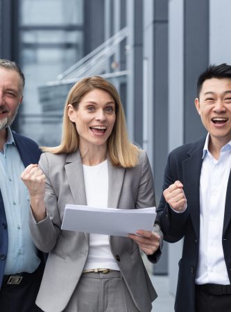 Businesswoman boss with her diverse team looking at the camera and rejoicing in success and victory, celebrating a successful contract a team of colleagues outside the office building with documents.